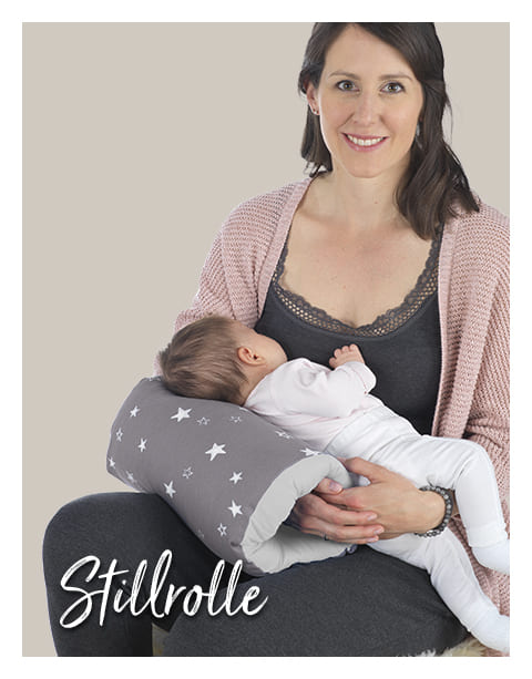 Eine Frau hält ein Baby, das auf einem grauen Kissen mit weißen Sternen liegt. Der Kontext ist ein neutraler, heller Hintergrund. Text: \