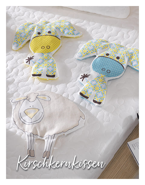 Auf dem Bild liegen drei Kirschkernkissen auf einer weißen, gesteppten Oberfläche.
Zwei der Kissen sind tierförmig, mit großen Ohren und süßen Gesichtern.
Das linke Tier hat ein gelbes Gesicht und ein kariertes Muster in Blau, Gelb und Weiß.
Das rechte Tier hat ein blaues Gesicht und das gleiche karierte Muster.
Das dritte Kissen unten ist in Form eines Schafs, beige mit braunen Linien für Gesicht und Beine.